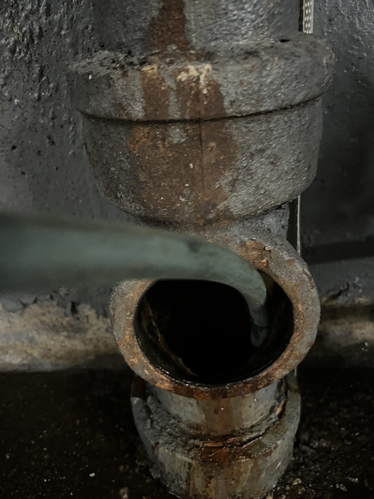 Corroded cast iron sewer cleanout hub with a drain cable inserted.